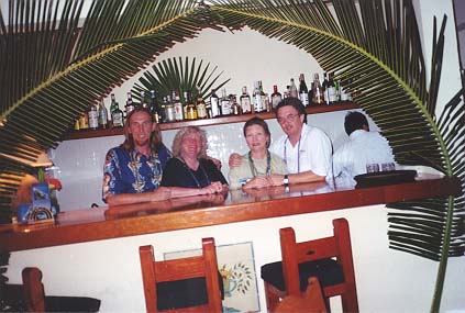 Jim, Deborah, Liz and Dennis pose behind the restaurant bar decorated with crossed palms.