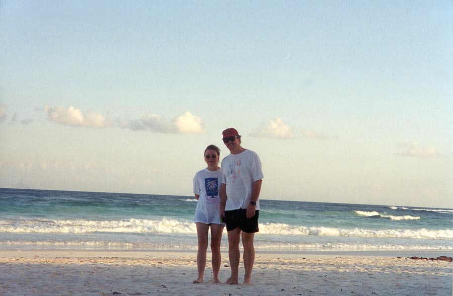 Liz and Dennis hand in hand with waves crashing into the beach behind them.