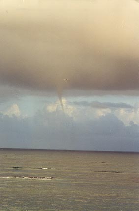 Thin tornado-like funnel cloud reaches down from the clouds toward the sea.